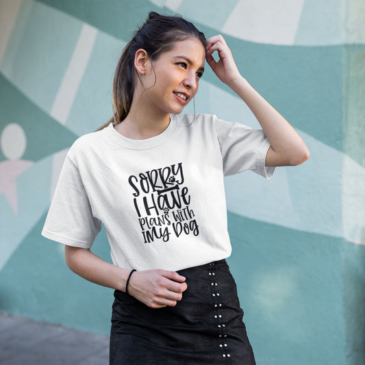 Woman wearing a white t-shirt with text, standing against a light blue wall.